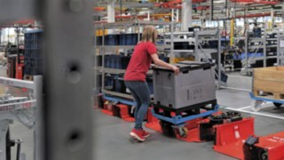 Bedienerin belädt einen Routenzuganhänger mit einem Trolley in Halbgröße